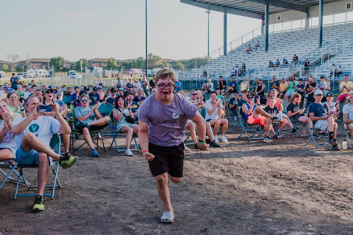 Athlete in purple shirt running with joy during Gravel Worlds race event, with crowds of spectators watching from lawn chairs in background