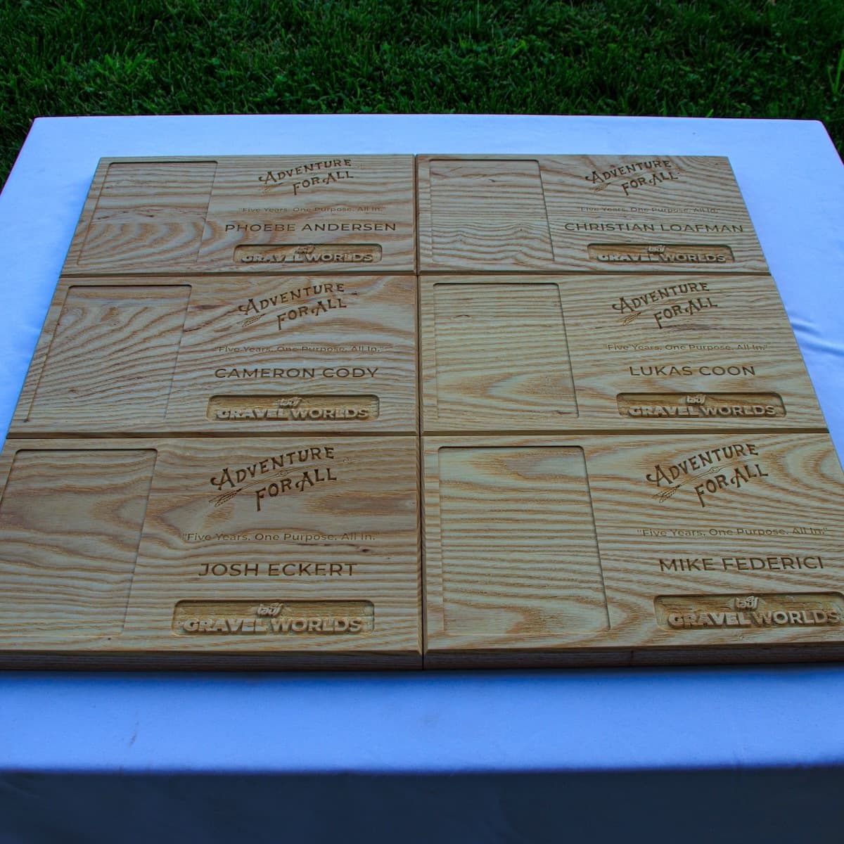 Six CNC-carved ash wood trophy plaques arranged in a grid, each personalized with different athlete names for the Adventure for All Gravel Worlds 2025 competition.