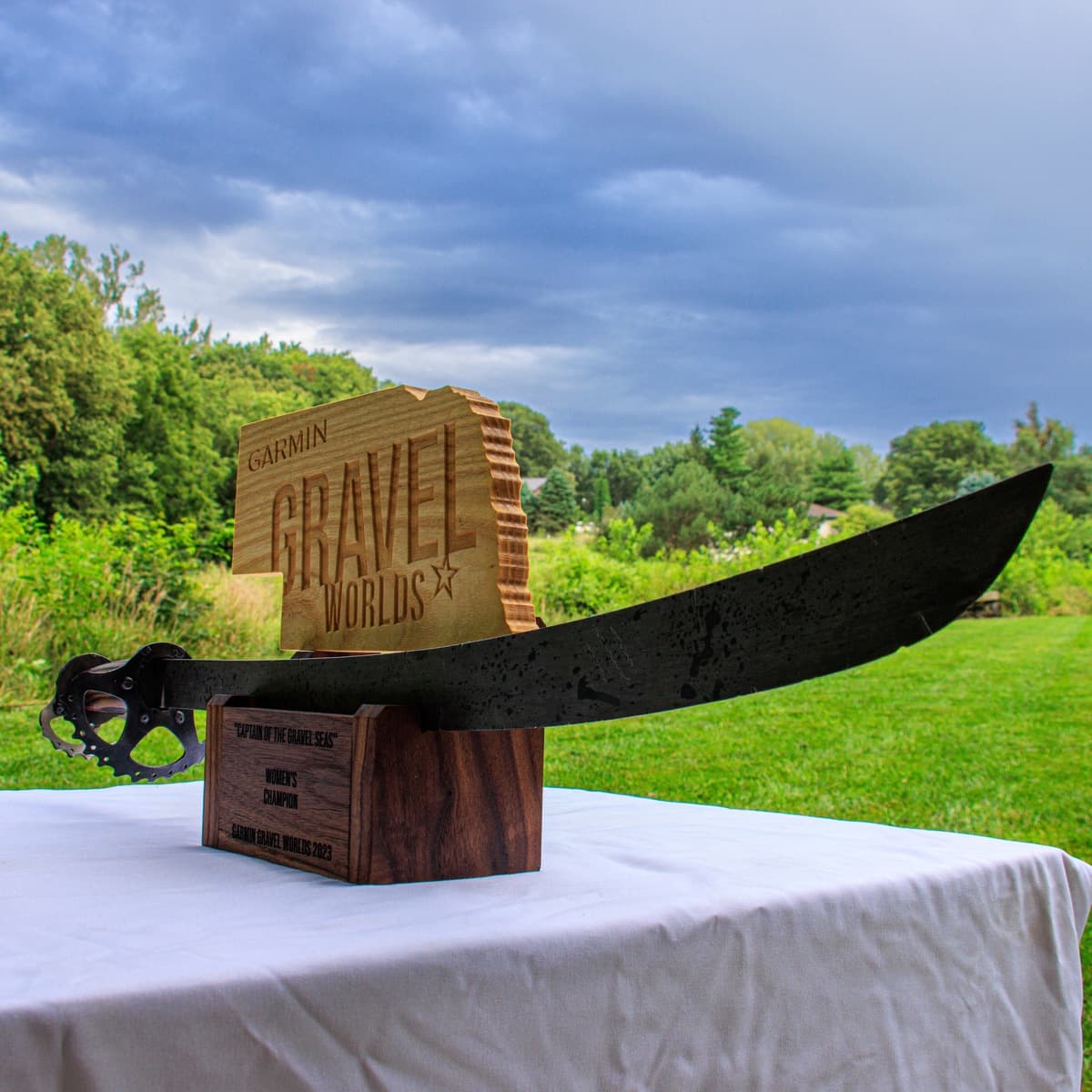 Gravel Worlds trophy plaque featuring "CAPTAIN OF THE GRAVEL SEAS" title and women's champion engraving on dark wood base with sword holder and metal handle detail
