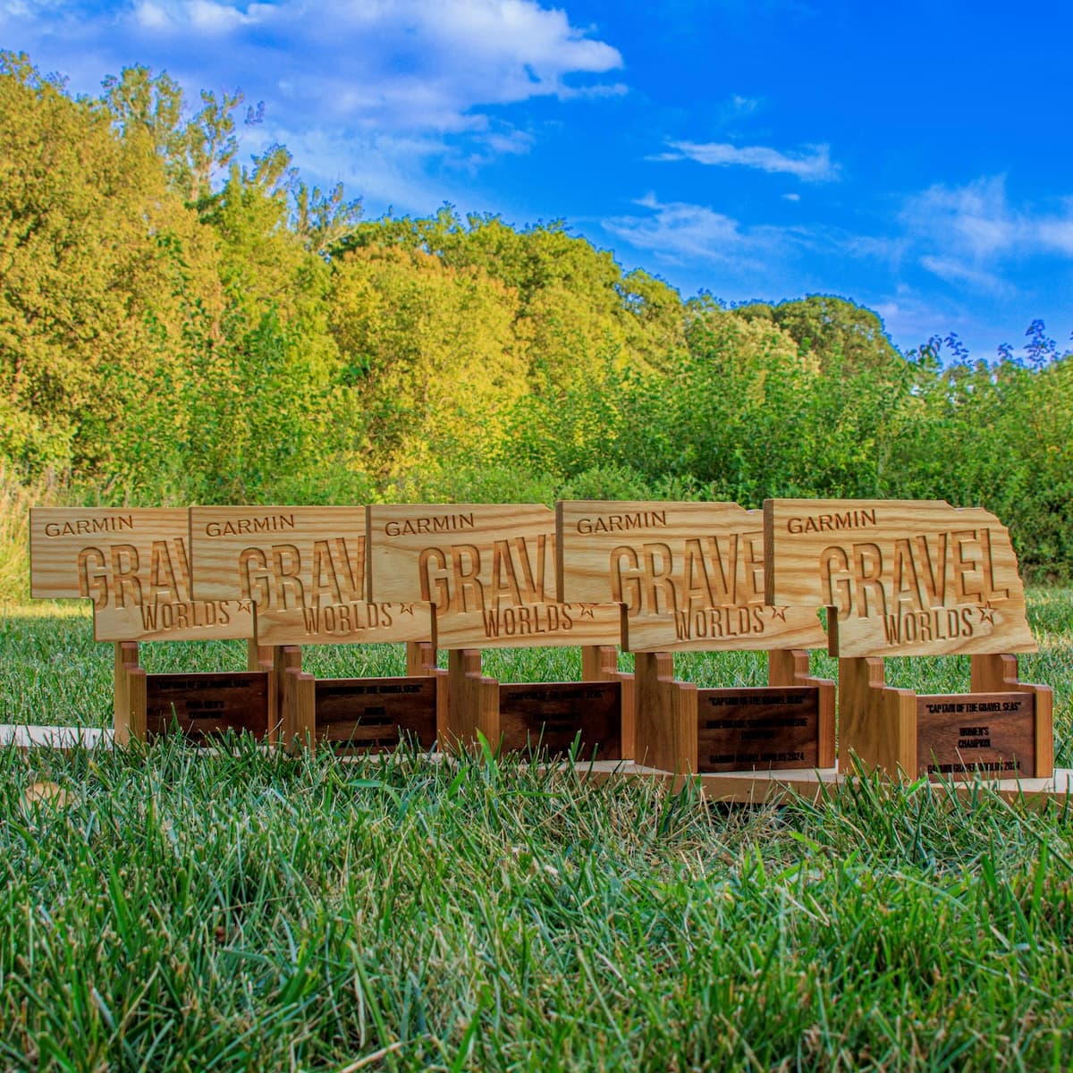 Five Garmin Gravel Worlds trophies displayed horizontally against a blue sky and trees background