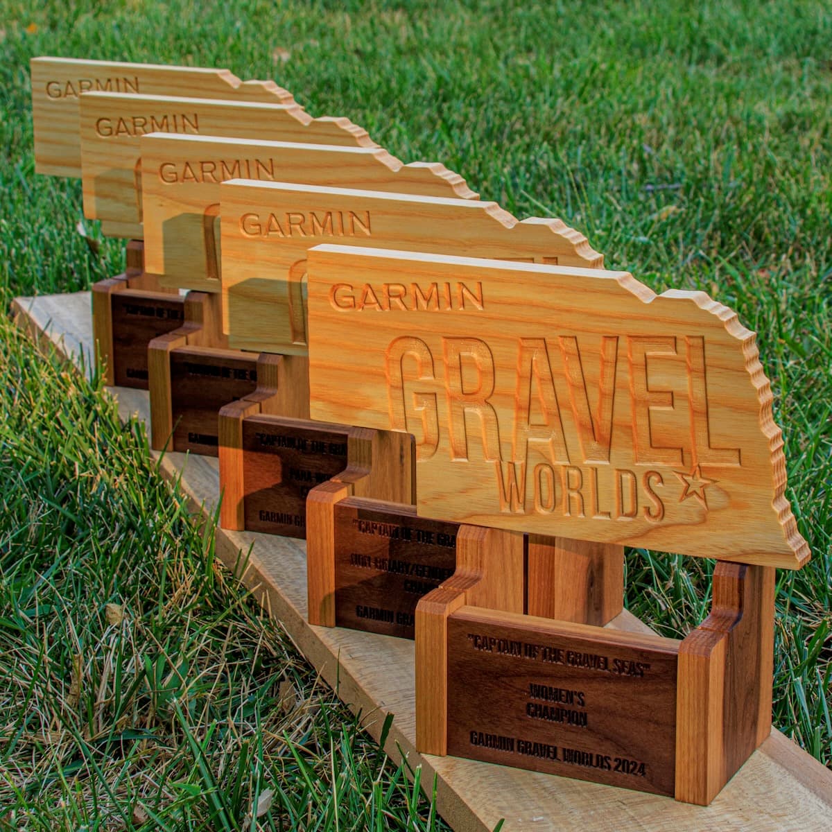 Perspective view of five Garmin Gravel Worlds trophies receding into distance, showing the progressive scale with detailed engraved plaques