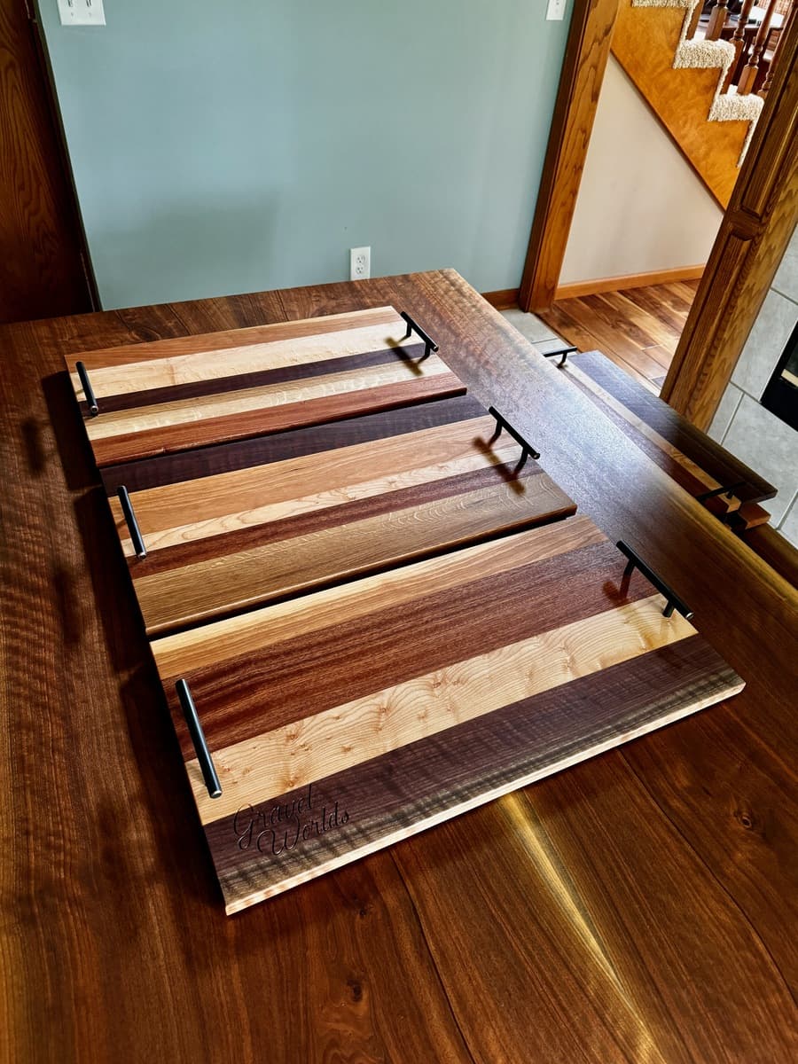 Display of multiple finished Gravel Worlds number plate holder plaques in home interior, showing varied wood species and finishes arranged with handles visible