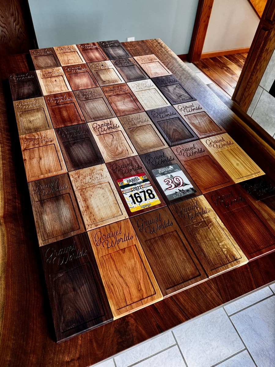 Detail view of multiple Gravel Worlds number plate plaques showing engraved text, wood grain patterns, and number plate examples (1678, 39) with metal plate inserts