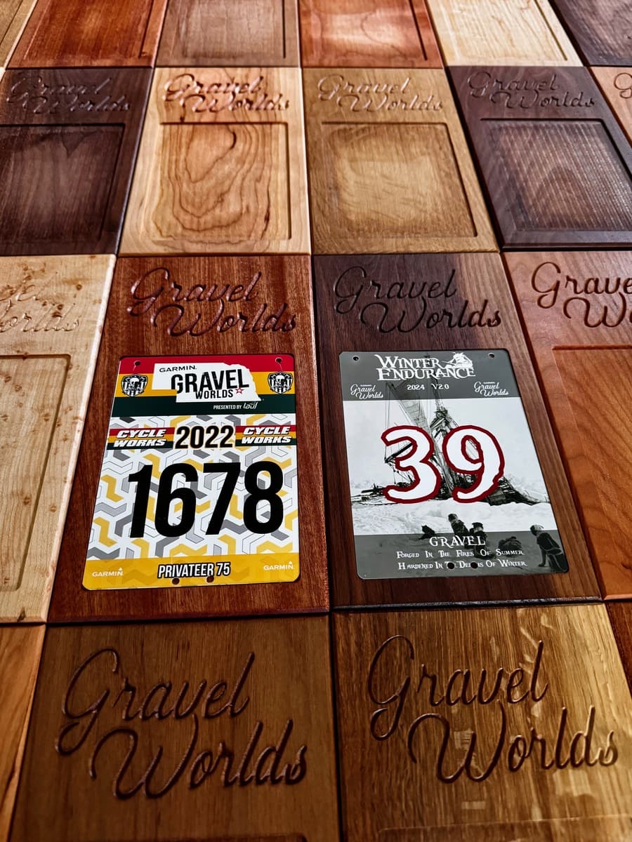 Large scale overhead display of approximately 40 Gravel Worlds wooden number plate holder samples in various wood species and stain colors arranged in rows