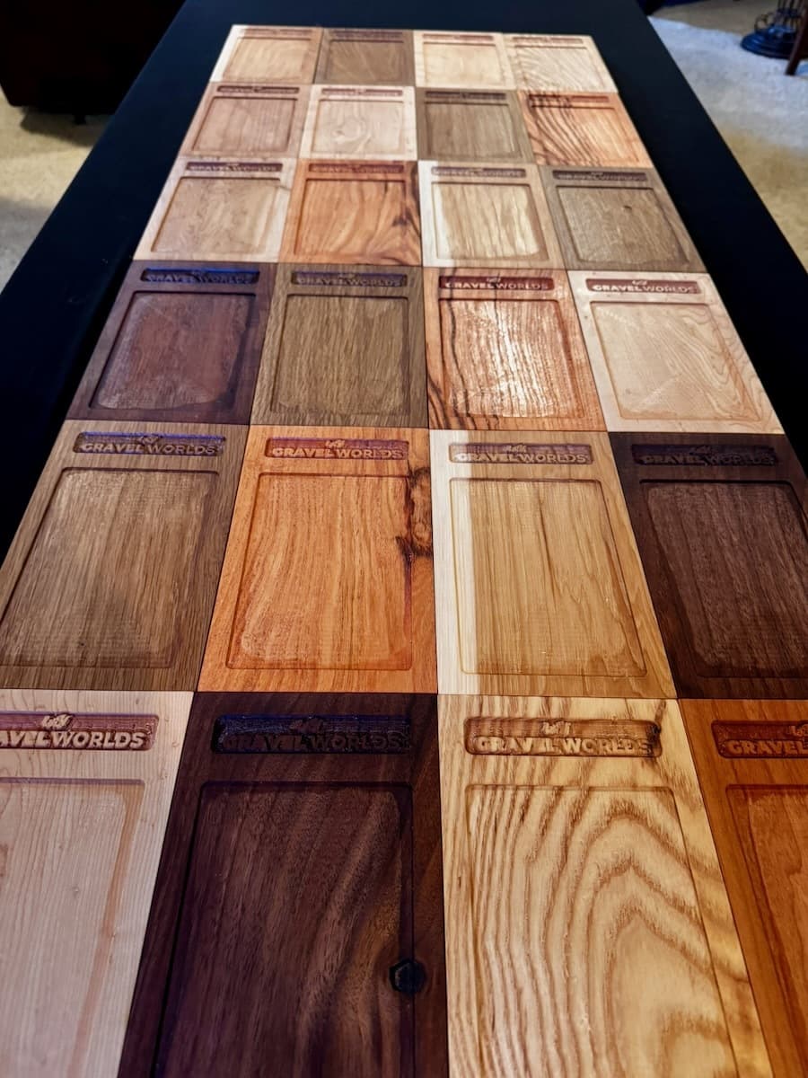 Grid display of sixteen wooden trophy plaques showing six different wood species and finishes for Gravel Worlds raffle options
