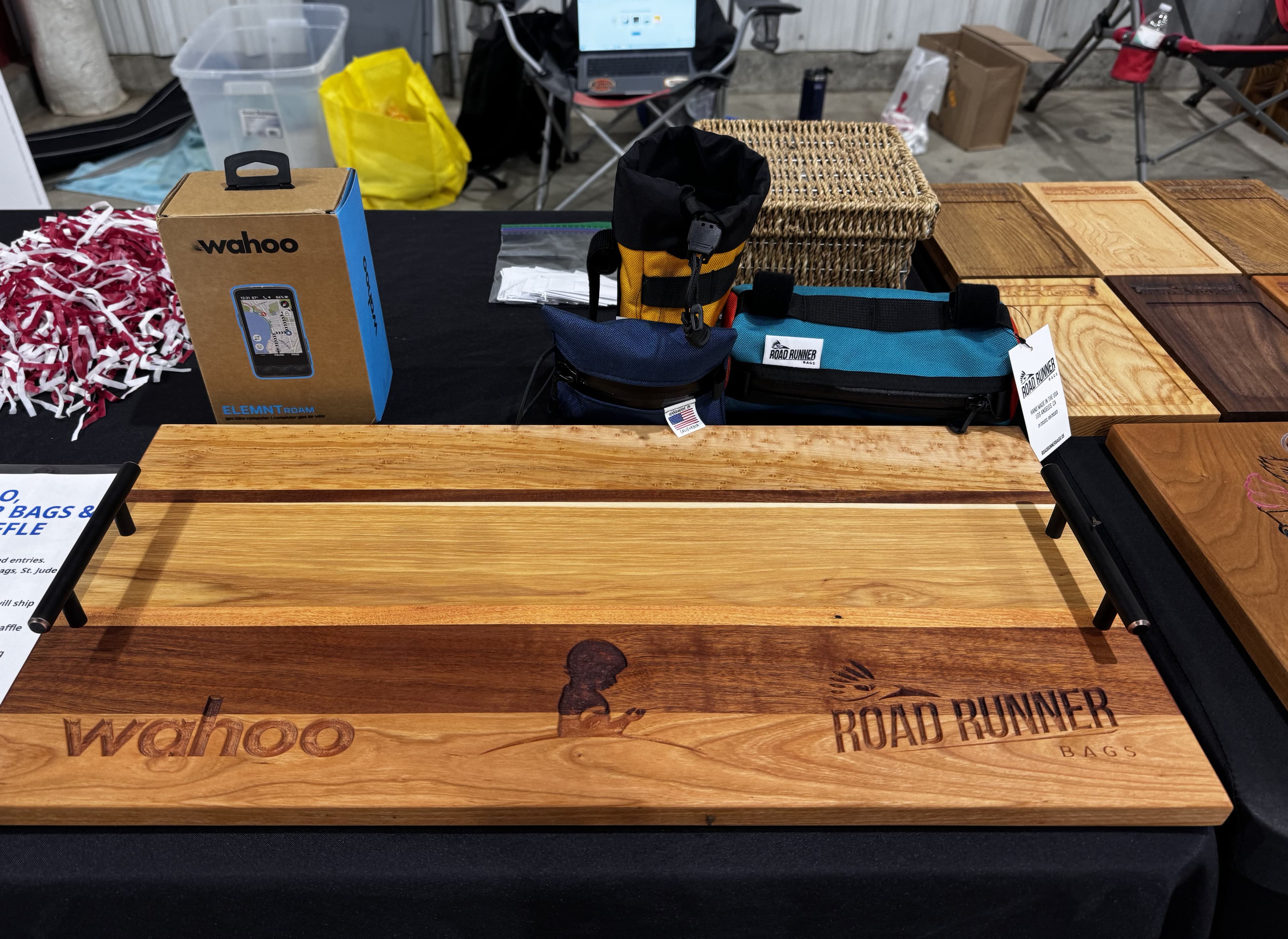 Two female cyclists at Gravel Worlds Expo holding wooden number plate holder plaques and displaying their raffle ticket numbers 4003 and 4002