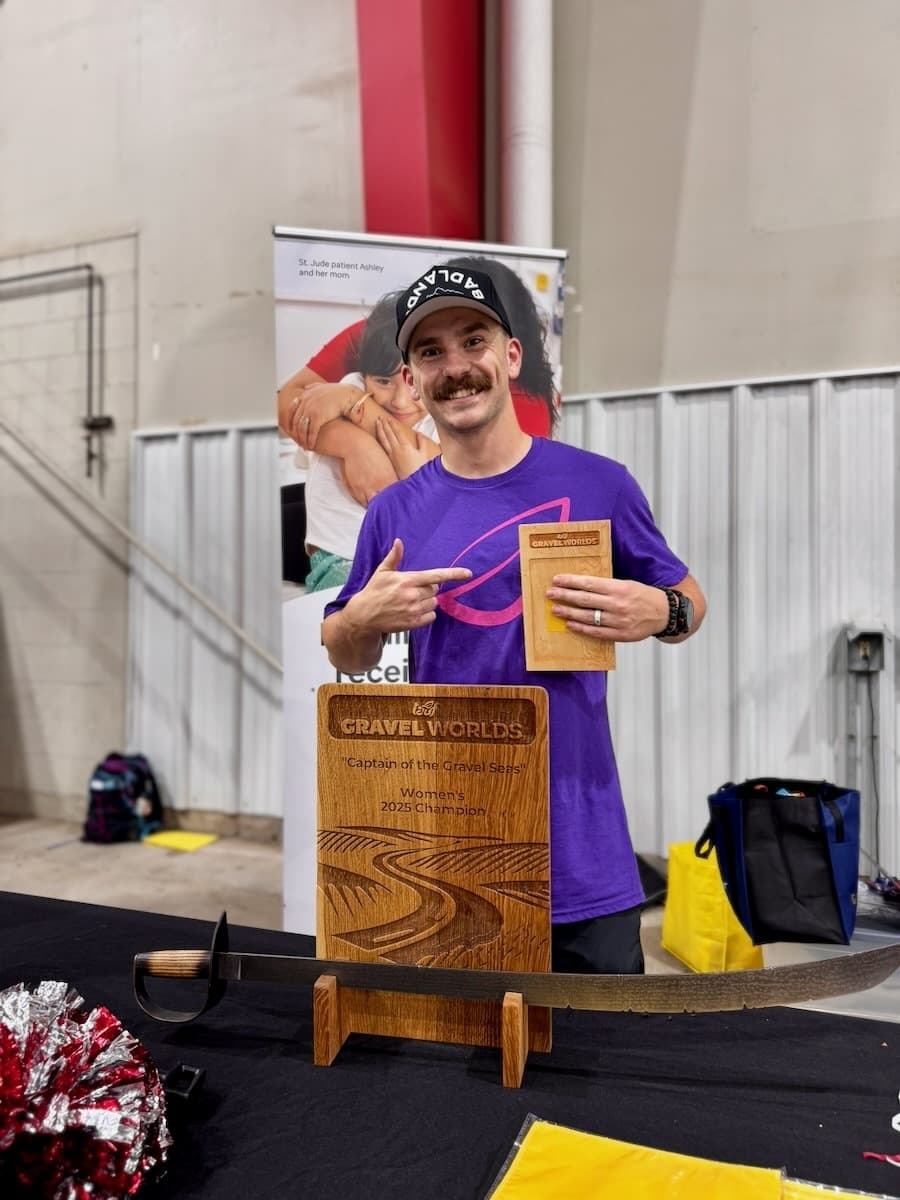 Attendee holding a wooden Gravel Worlds Women's 2025 Champion trophy plaque with detailed engraving