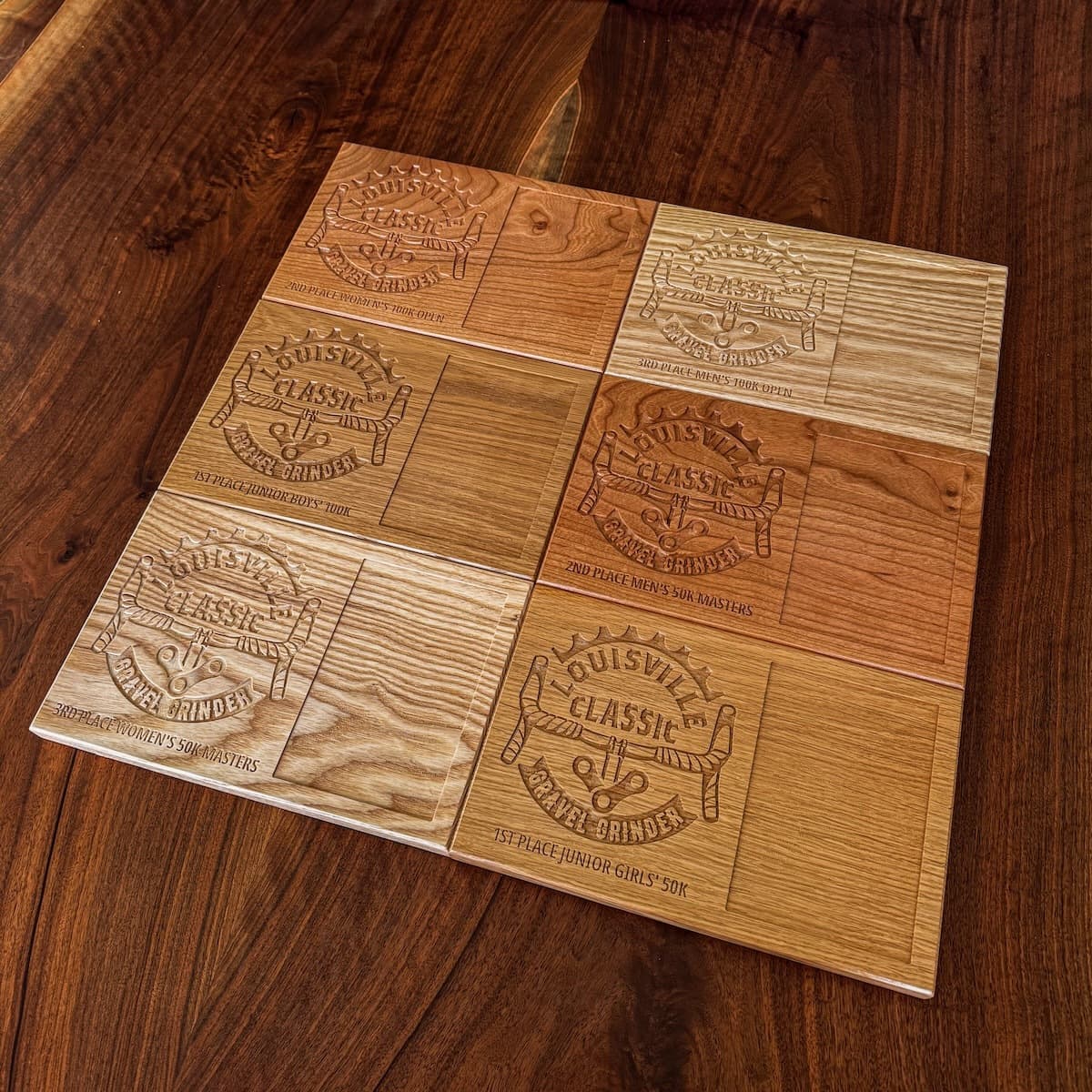 Collection of white oak, cherry, and ash trophy plaques arranged on wooden surface showing engraved Louisville Classic branding and category winners