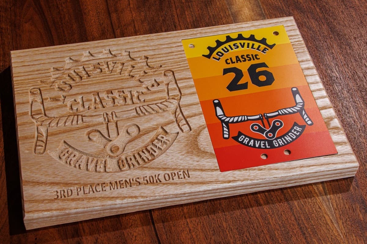 Ash wood trophy plaque with engraved Louisville Classic logo and sword graphic showing 3rd place men's 50k open race result with orange number plate holder