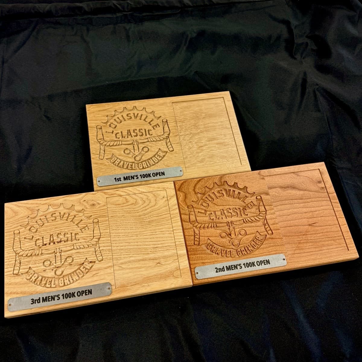 Three CNC-carved white oak and cherry wood trophy plaques for Louisville Classic Gravel Grinder arranged together on dark background