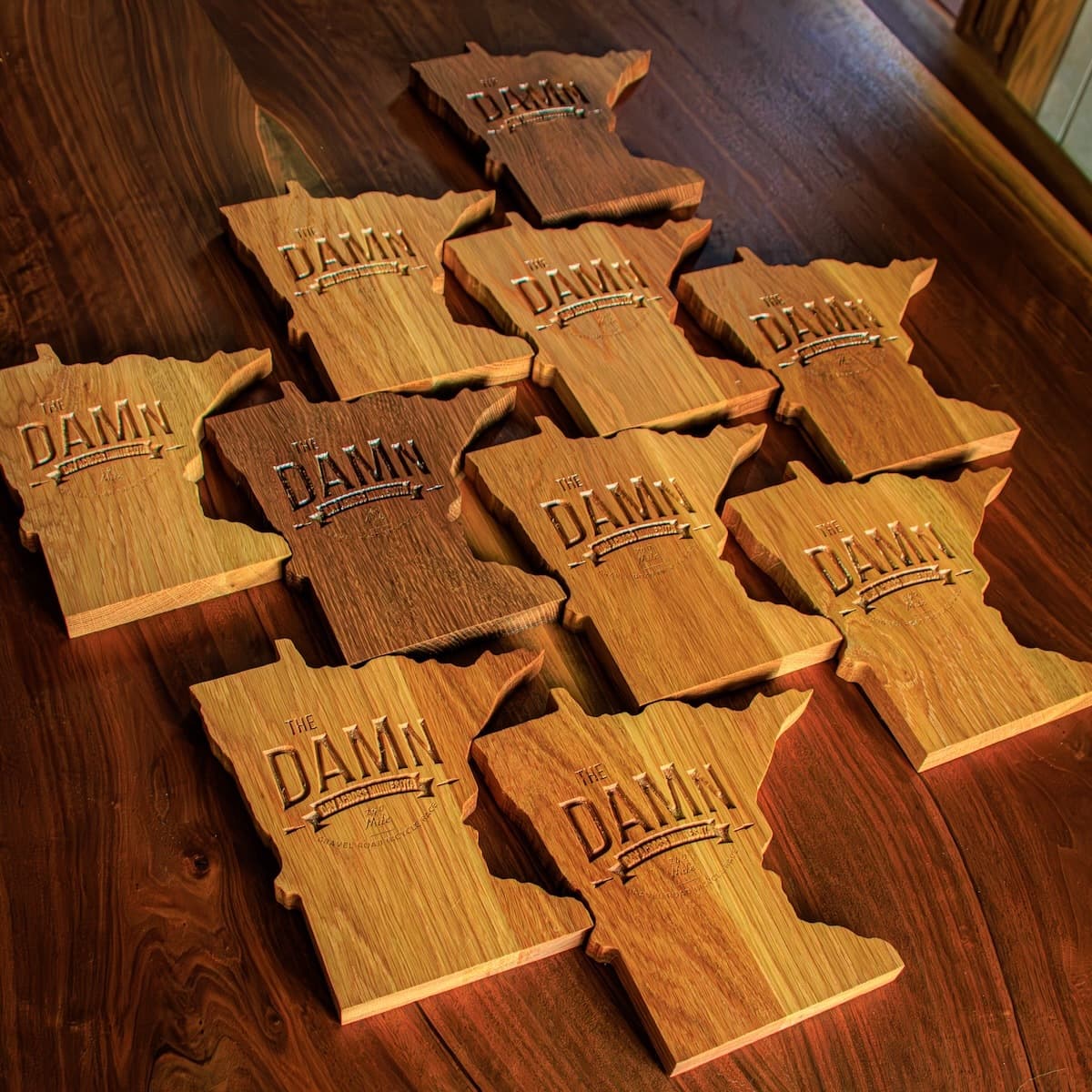 Collection of finished white oak DAMn trophy plaques arranged on a wooden surface, showing engraved text and design details for multiple winners