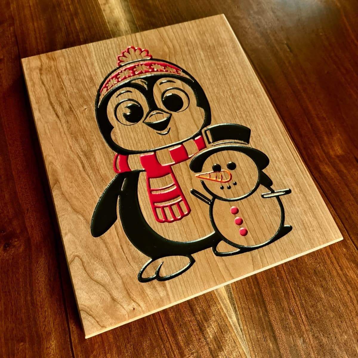 Cheerful penguin and snowman wall art on cherry with hand-painted details—penguin wearing red and tan striped scarf with Christmas hat, snowman wearing top hat