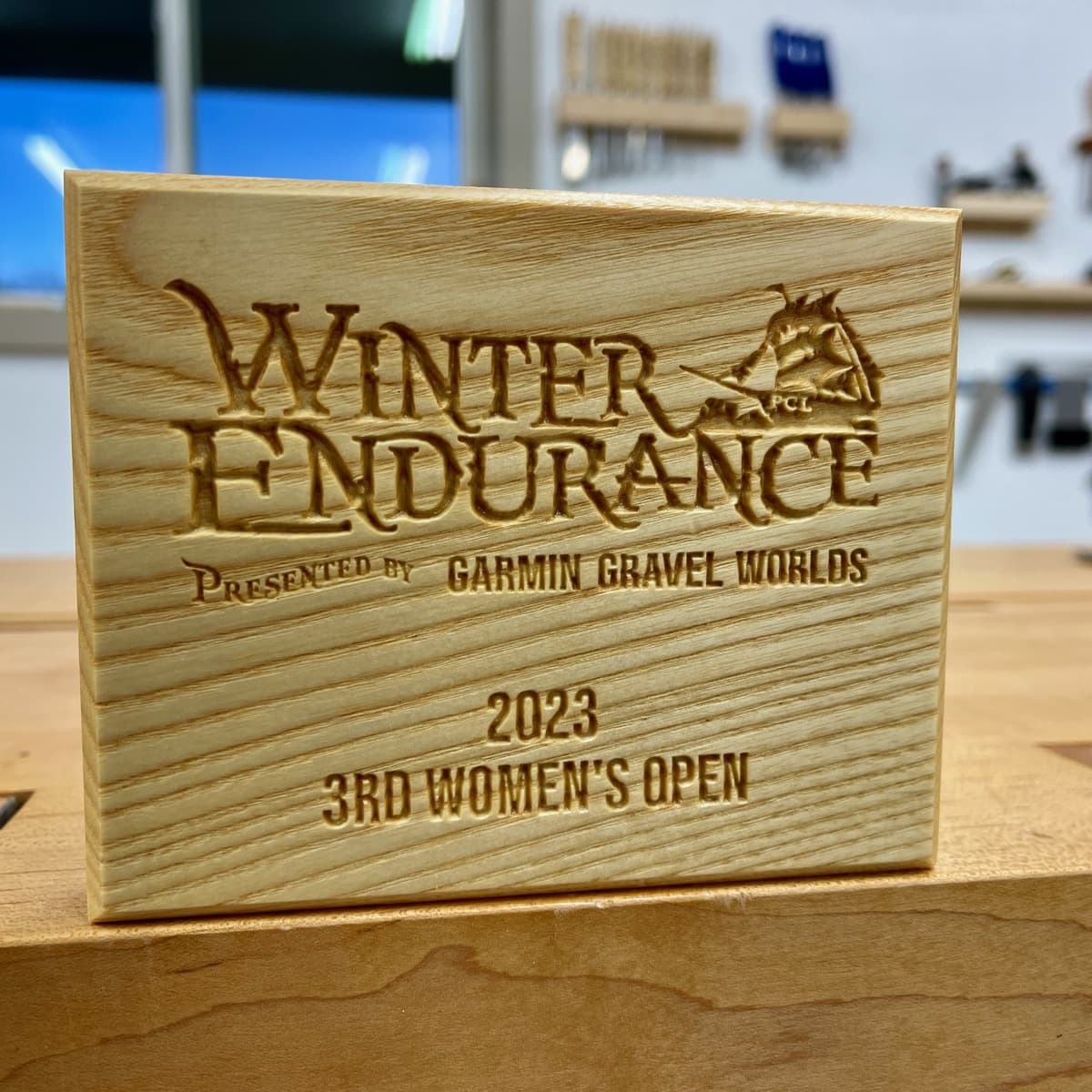 Three rows of Winter Endurance trophies arranged on display table showing different wood species—dark walnut in back row, light ash in center, and medium cherry in front—with engraved text and race category details
