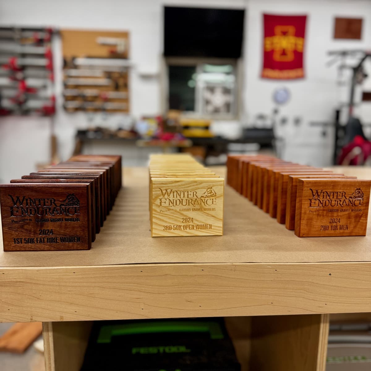 Three rows of Winter Endurance trophies arranged on display table showing different wood species—dark walnut in back row, light ash in center, and medium cherry in front—with engraved text and race category details
