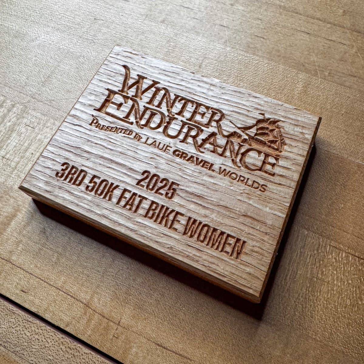 Light-stained wood Winter Endurance trophy plaque with CNC engraving showing 2025 Third Place 150K Fat Bike Women's race award