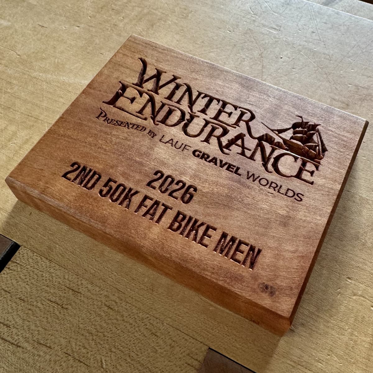 Winter Endurance 2026 wooden trophy plaque with CNC-engraved text showing Second Place 50K Fat Bike Men race category and Lauf Gravel Worlds branding on walnut-toned wood