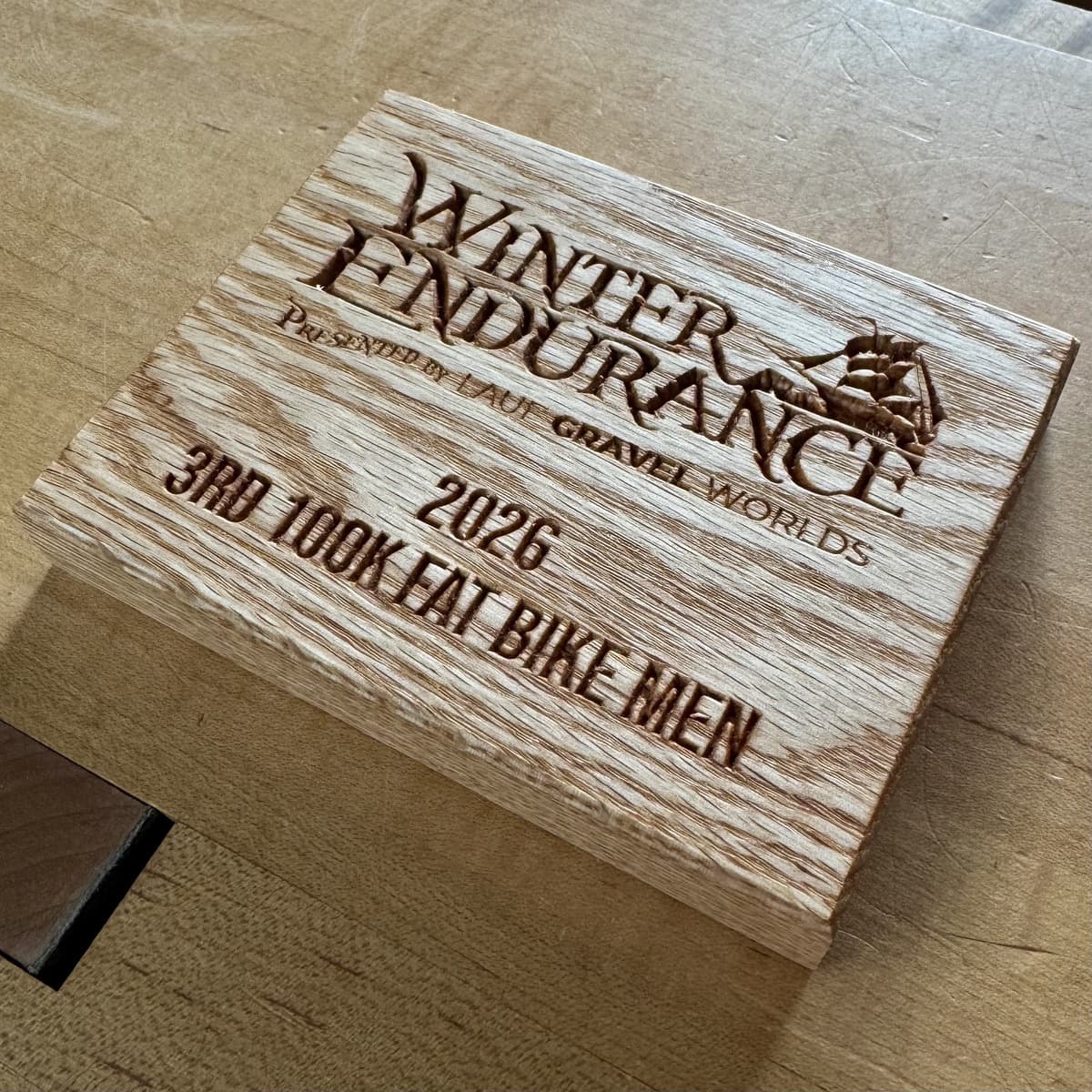 Winter Endurance 2026 wooden trophy plaque with distinctive light wood grain pattern and CNC-engraved text showing Third Place 100K Fat Bike Men race award with event branding