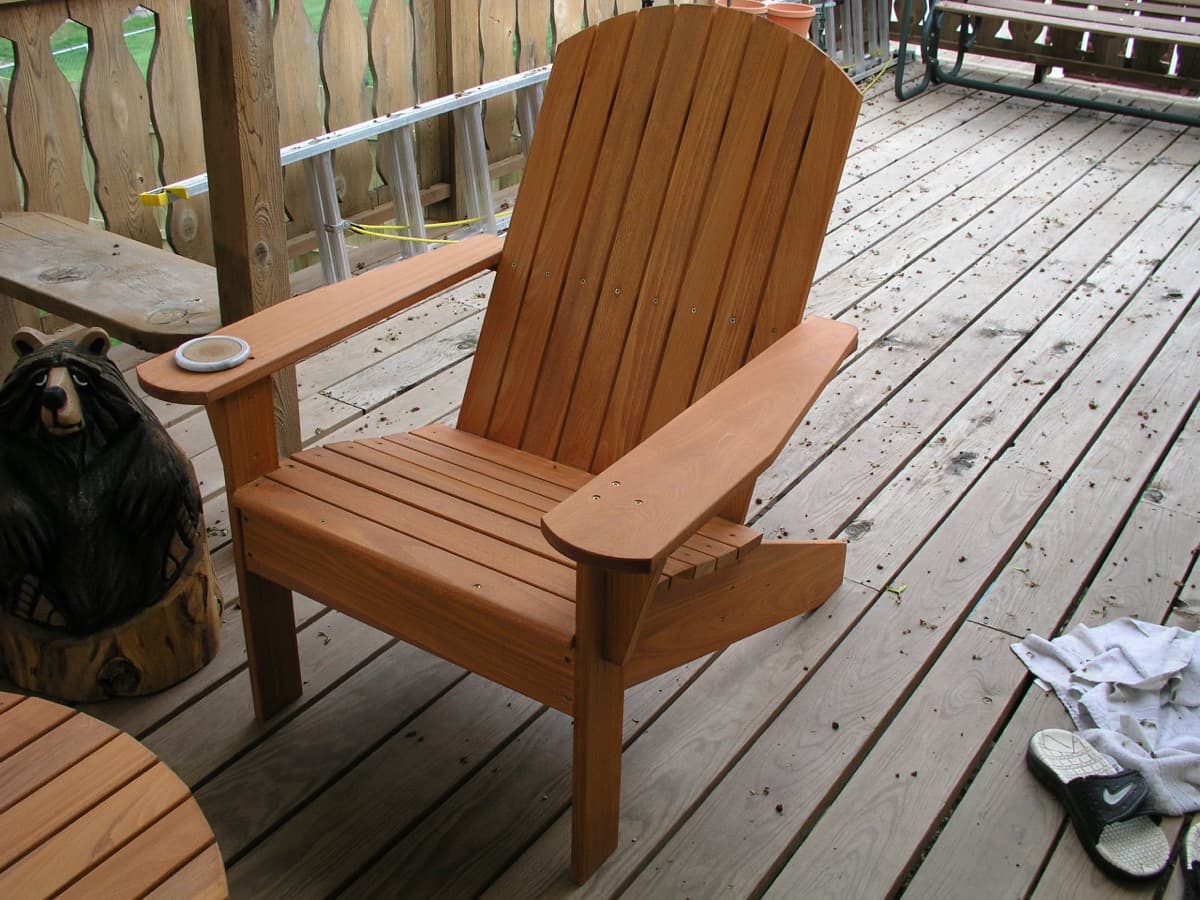 Single cypress adirondack chair photographed from side angle, showing curved backrest and wide armrests with medium stain finish