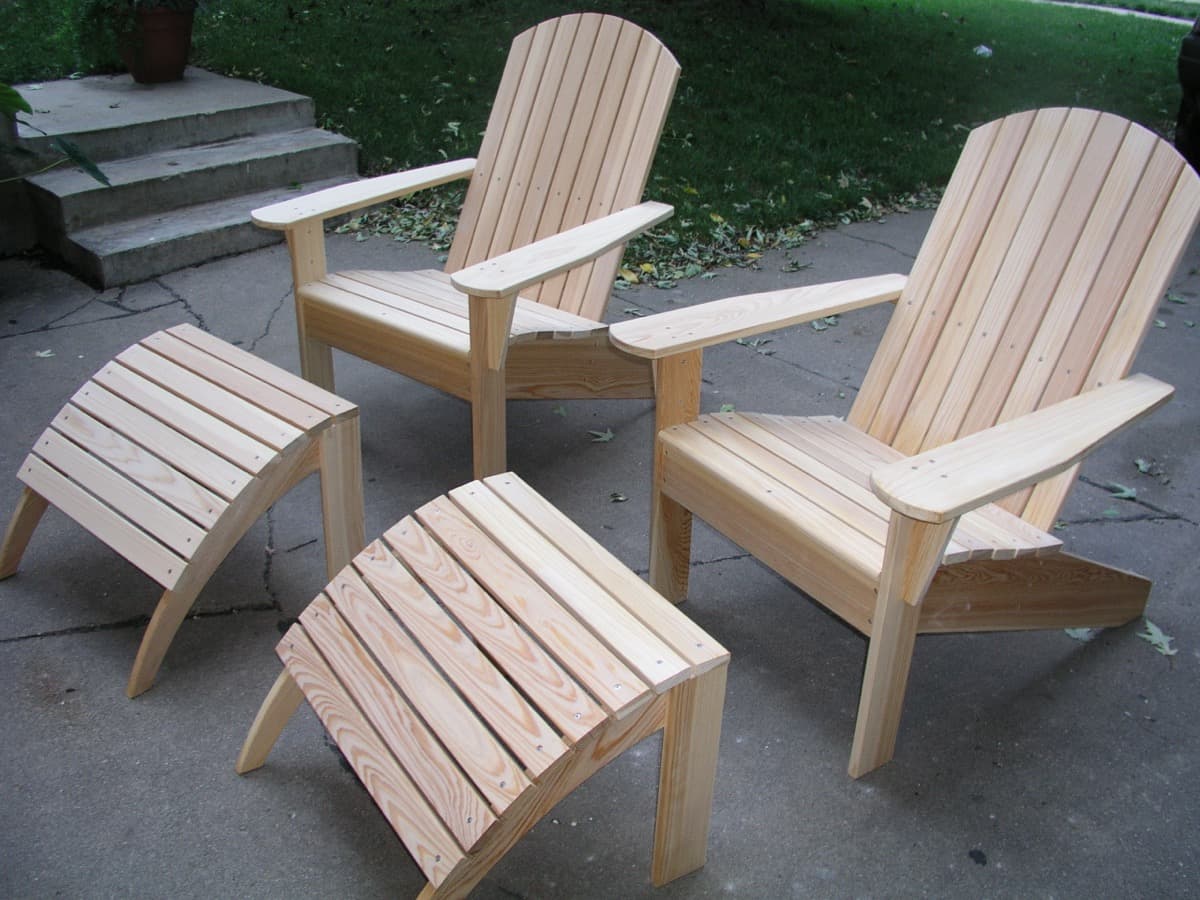 Three light-stained cypress adirondack chairs with matching footstools arranged on driveway, showcasing unfinished natural wood appearance