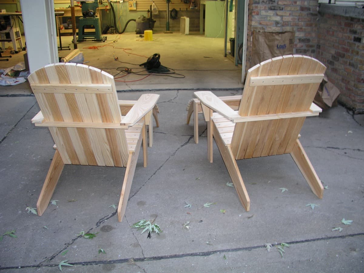 Two unfinished cypress adirondack chairs in workshop environment, showing raw wood grain and structural details before final finishing