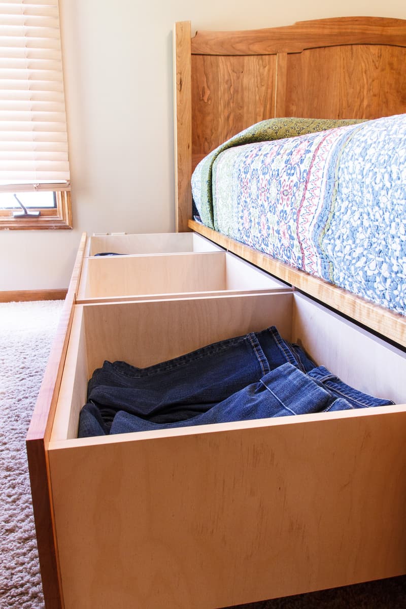 Cherry platform bed with storage drawer open showing blue jeans inside