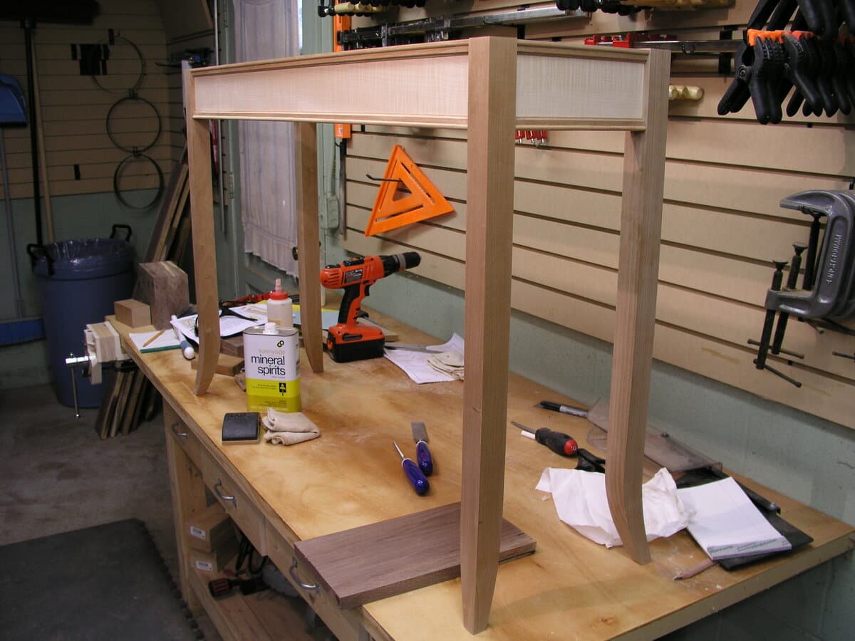 Partially assembled console table frame in workshop with workbench, showing mortise and tenon construction under development with tools visible