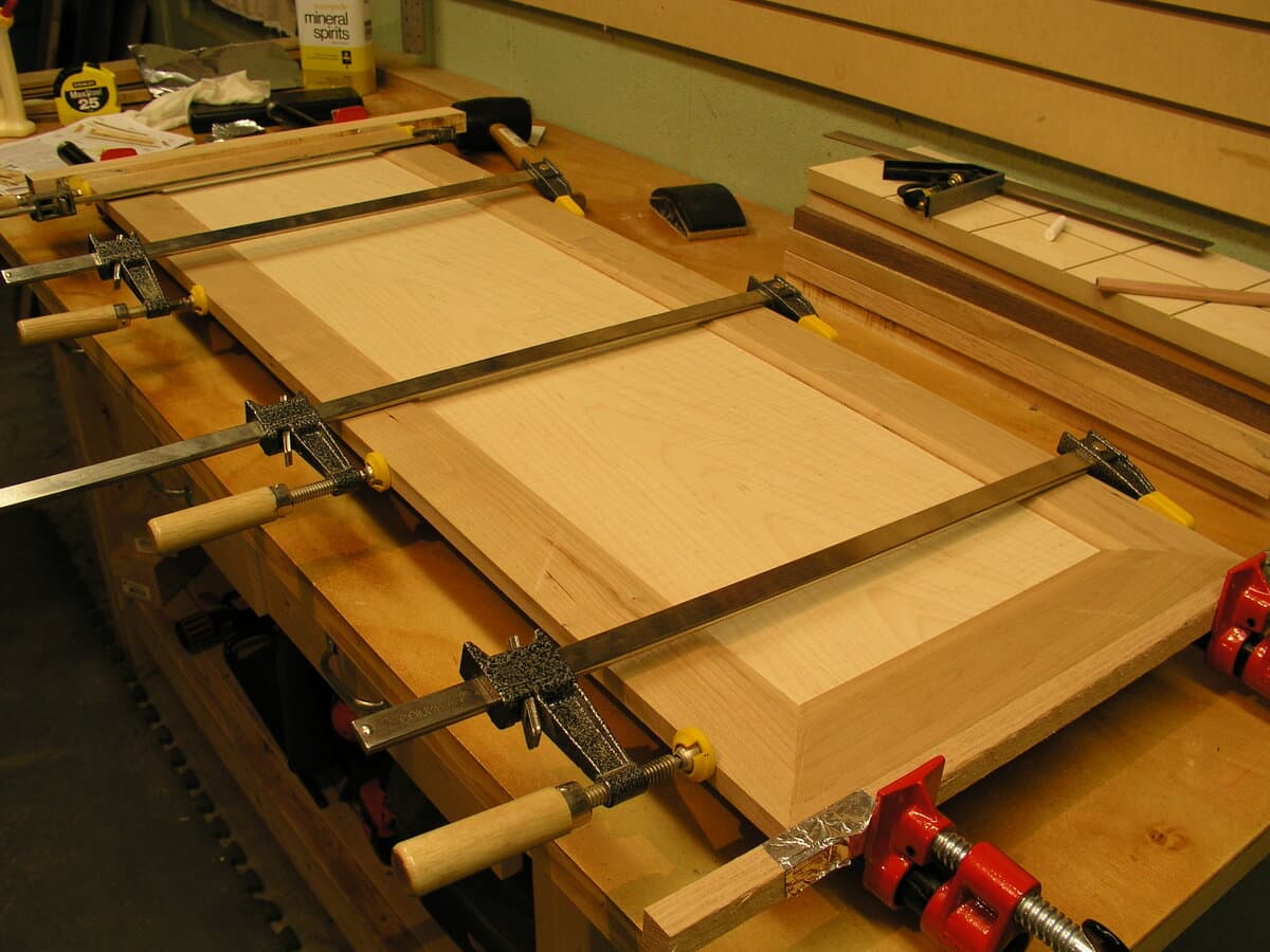Top view of curly maple table top under construction with multiple panel sections clamped together on workshop table