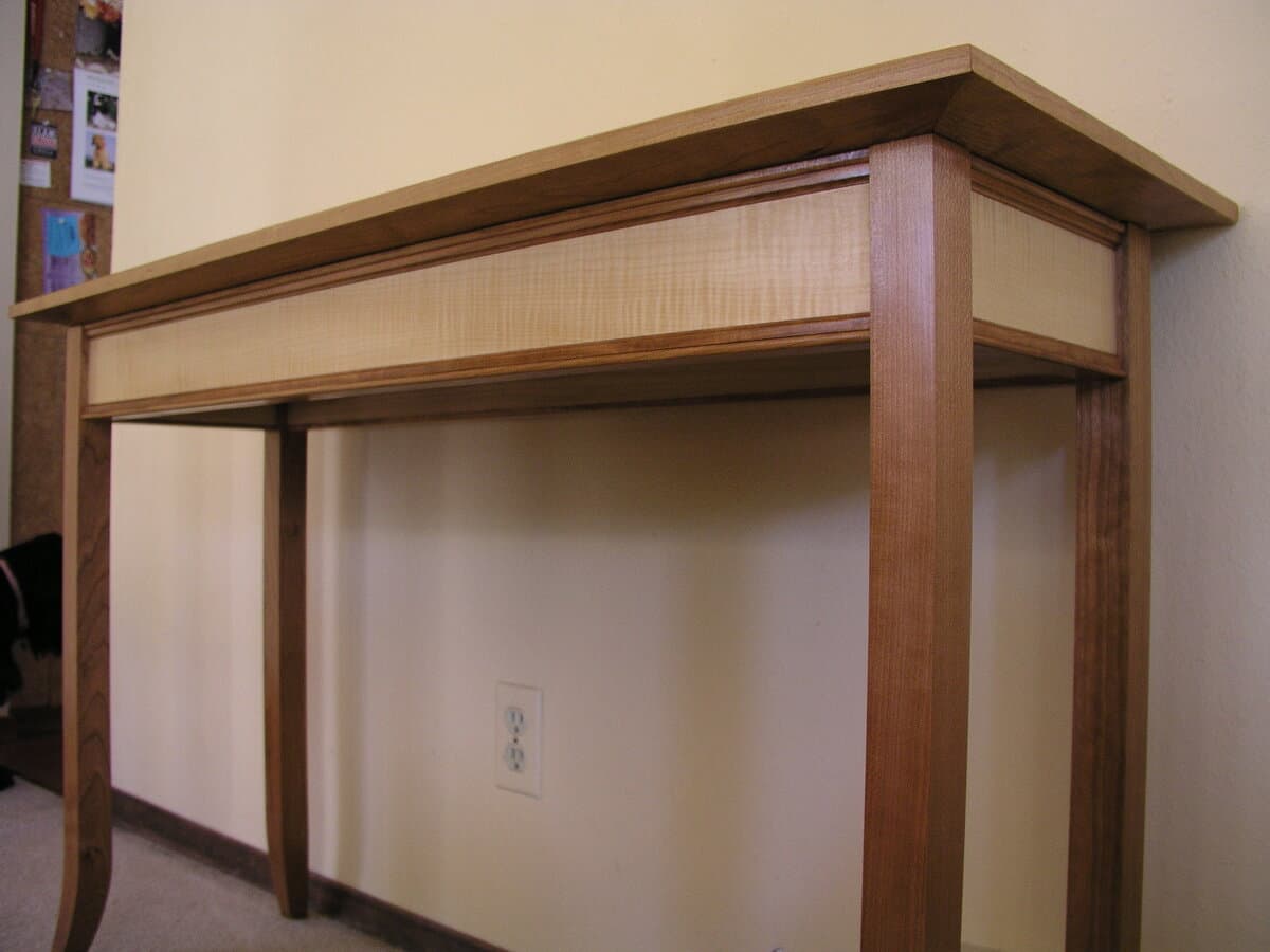 Side view of completed console table showing curved cherry legs and contrasting curly maple aprons with refined proportions and joinery