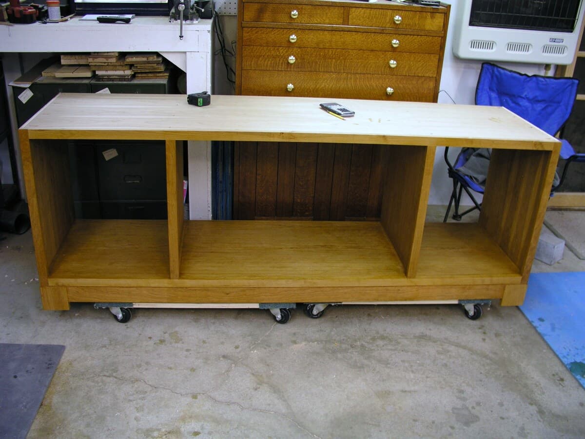 Finished cherry TV stand in workshop on casters showing complete three-compartment design with side doors and center shelf