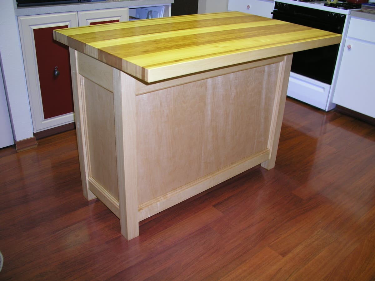 Completed kitchen island with cherry top and hard maple base in residential kitchen, featuring cabinet doors, drawers, and Waterlox finish