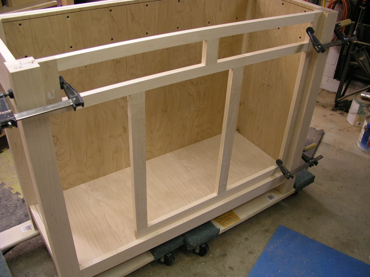 Kitchen island cabinet structure under construction showing hard maple frame and plywood cabinet sides with metal clamps during assembly