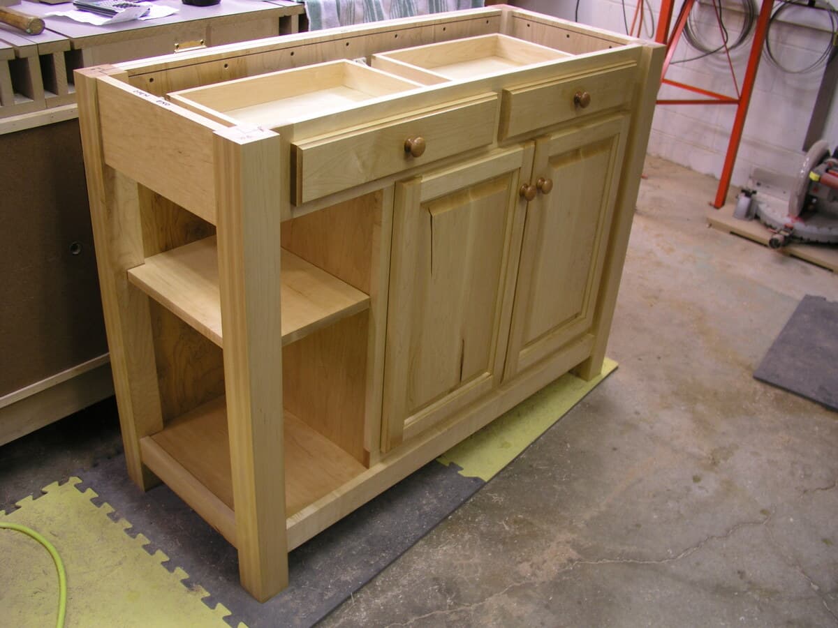 Finished kitchen island showing cherry top with contrasting hard maple base, cabinet doors with wooden knobs, and open shelf storage