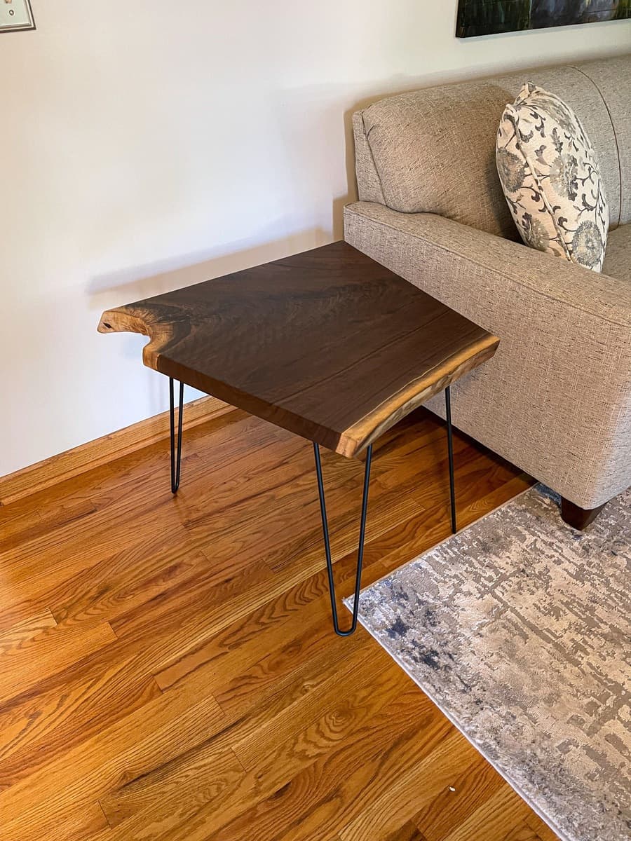 Live edge walnut end table styled in living room next to sofa showing the dramatic grain pattern and natural wood finish