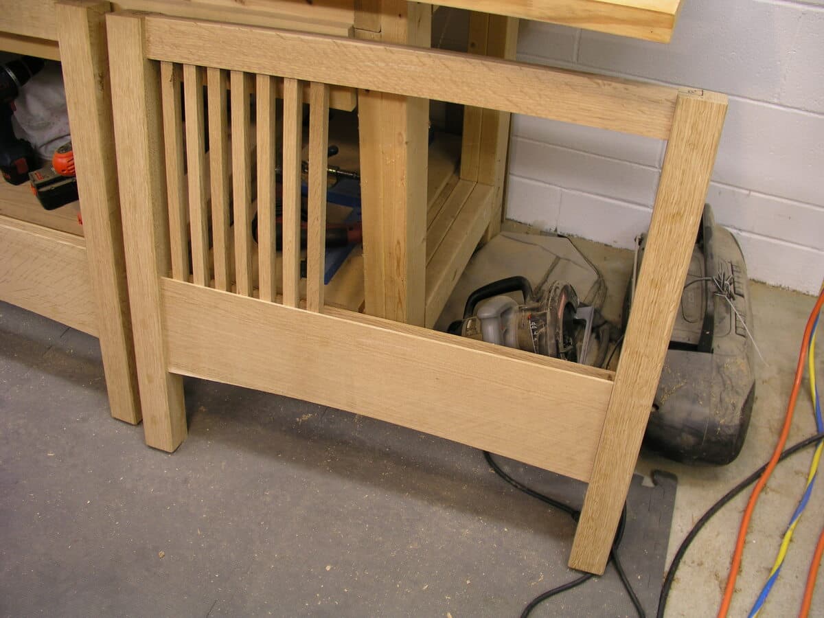 Dry-fit assembly of the Mission sofa frame components in the workshop. The raw white oak pieces show the characteristic vertical slat construction of the arms and back, with mortise and tenon joints visible before glue-up. This construction phase reveals the precision joinery that will be hidden in the finished piece.