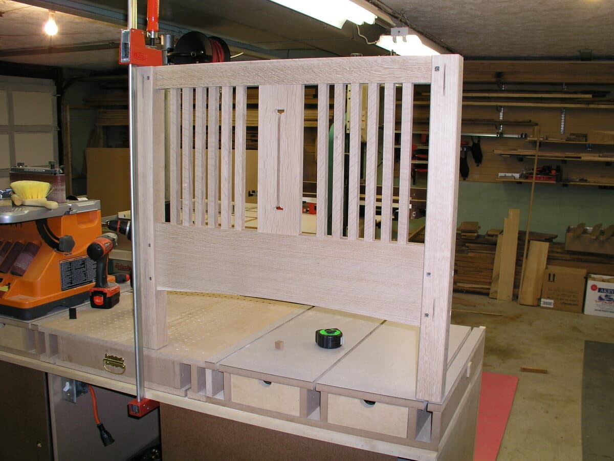 Workshop construction photo showing an assembled side panel unit standing upright. The raw quarter-sawn white oak frame displays the mortise and tenon joinery connecting the vertical slats to the rails. The unfinished wood shows the natural color of white oak before the Shellac and Waterlox finish is applied.