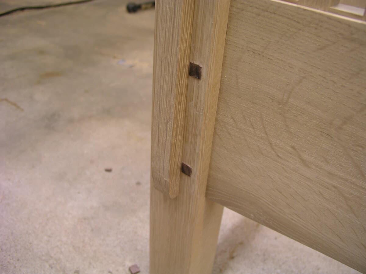 Close-up detail of walnut plugs installed in pre-drilled holes on the sofa arm. The dark walnut square plugs contrast against the lighter quarter-sawn white oak, creating a decorative accent typical of Mission furniture. This photo was taken before final finish application, showing the natural wood colors.