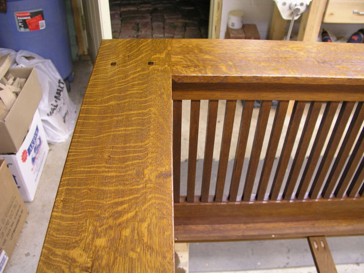 Close-up of finished mortise and tenon joinery at arm-to-rail connection with walnut plug detail. The rich amber finish showcases the quarter-sawn white oak's medullary rays, while the flush-mounted walnut plug adds traditional Mission-style ornamentation. The Shellac and Waterlox Satin finish provides a hand-rubbed appearance with excellent depth.