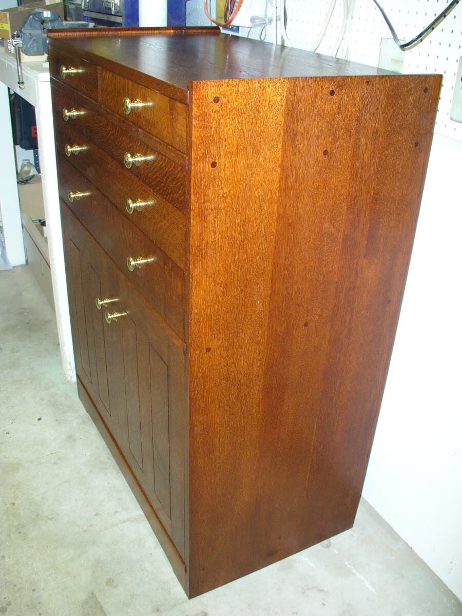 Rift and quarter-sawn red oak tool cabinet photographed in workshop, showcasing the striking grain patterns on the cabinet side with visible wood figure characteristic of quarter-sawn oak. The cabinet features brass hardware pulls and a satin finish from Shellac and Waterlox.