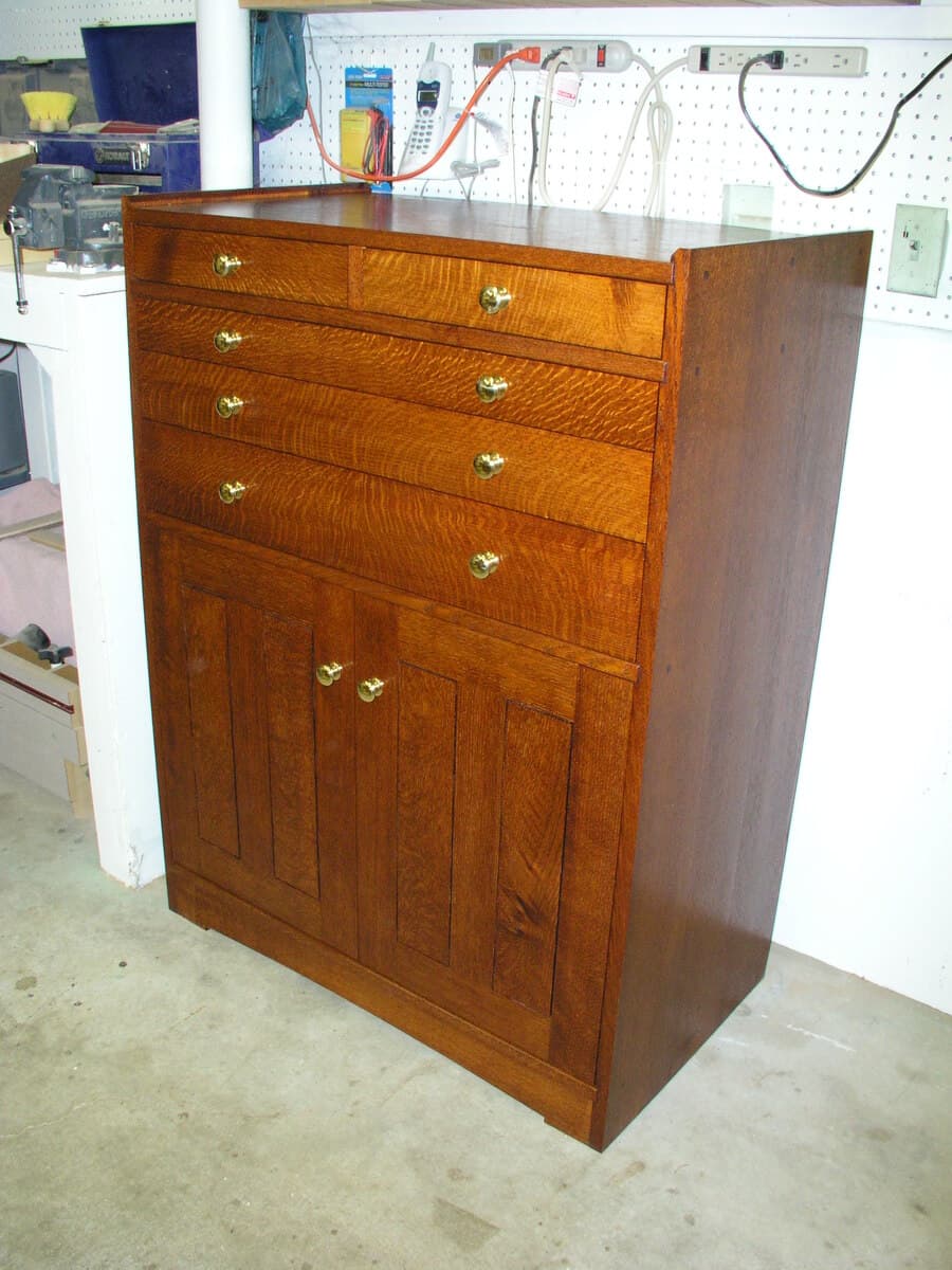 Workshop photo of the completed red oak tool cabinet displaying the full front elevation with drawers across the top section and paneled door storage below, finished with Shellac and Waterlox Satin. The consistent grain and finish quality is evident across all surfaces.