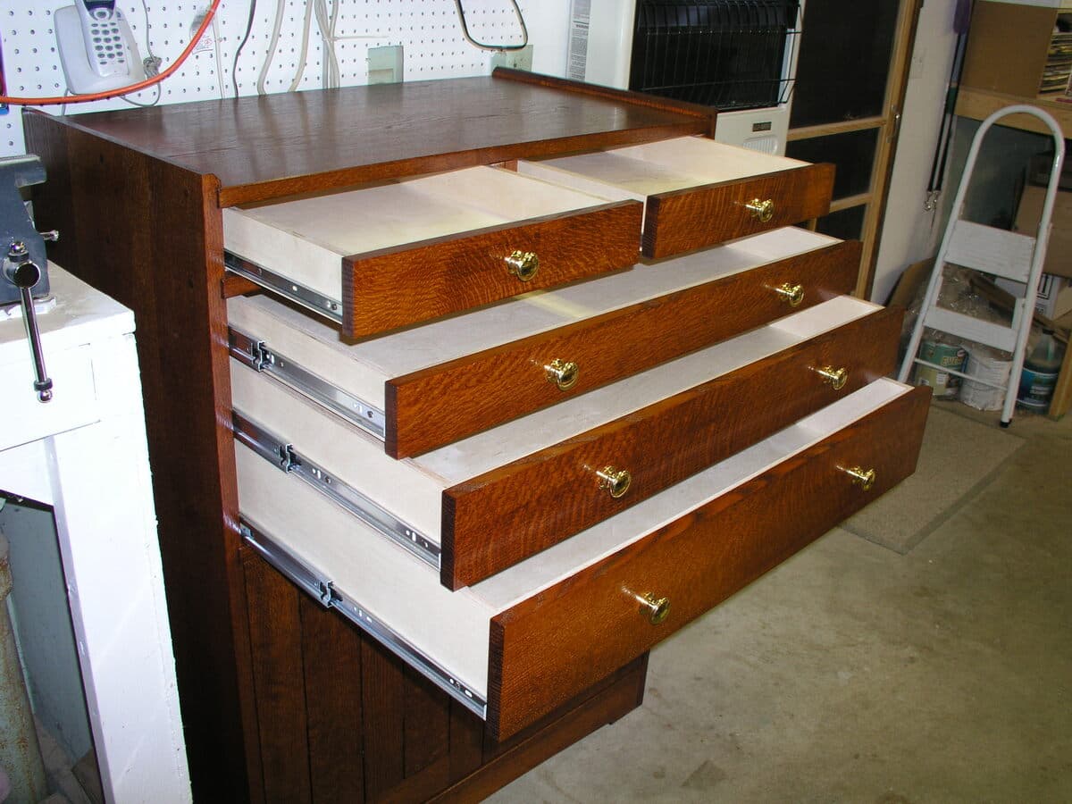 Cascading open drawers showcasing the tool cabinet's five-drawer configuration with brass pulls and full-extension slides, displaying the dramatic quarter-sawn oak grain and rich Shellac and Waterlox Satin finish throughout the exterior and light wood drawer box construction.