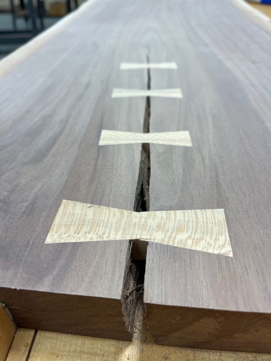End view of walnut console table showing four light-colored sycamore bowties flush-installed across natural crack, demonstrating structural repair and decorative craftsmanship on finished tabletop.