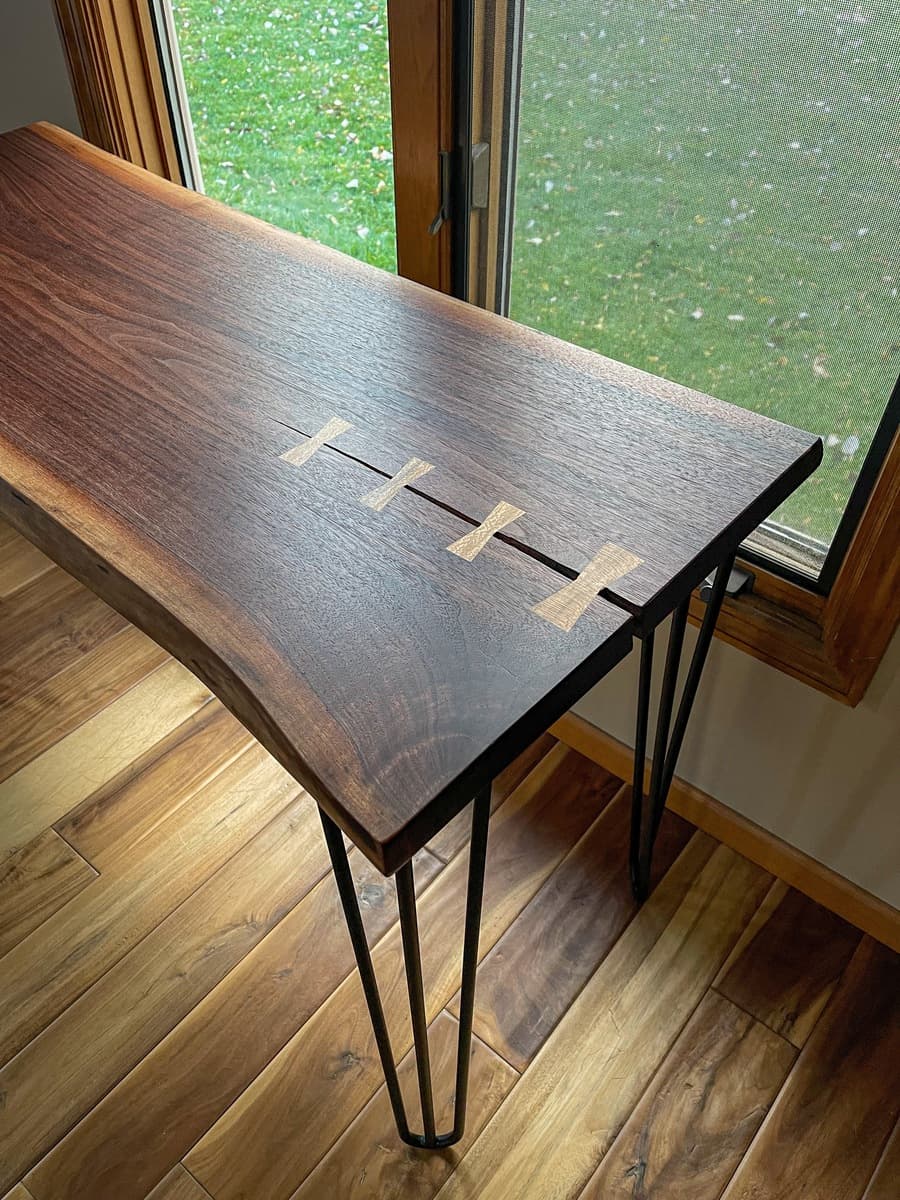Overhead angled view of walnut console tabletop showing four evenly-spaced sycamore bowtie inlays across natural crack, highlighting contrast between dark walnut and light sycamore wood.