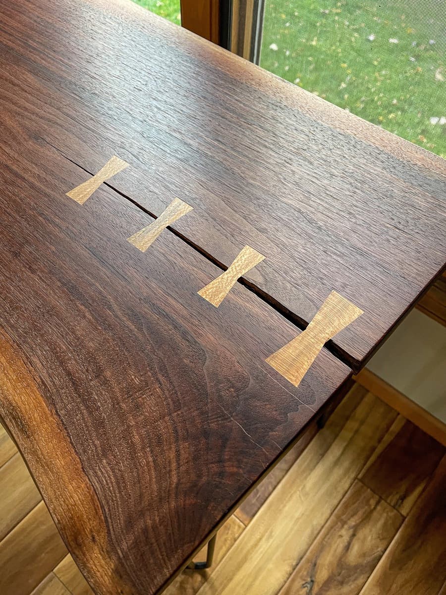 Close-up detail of walnut tabletop surface showing four sycamore bowtie inlays in diagonal crack, emphasizing wood grain figuring, finished surface, and precise inlay craftsmanship.