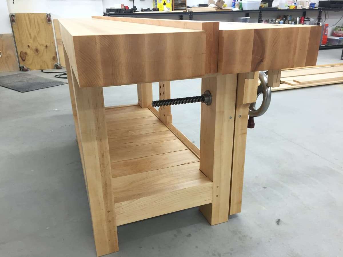 Underside view of Roubo workbench showing slatted maple shelf, leg vise mechanism with threaded rod, and mortise-and-tenon joinery