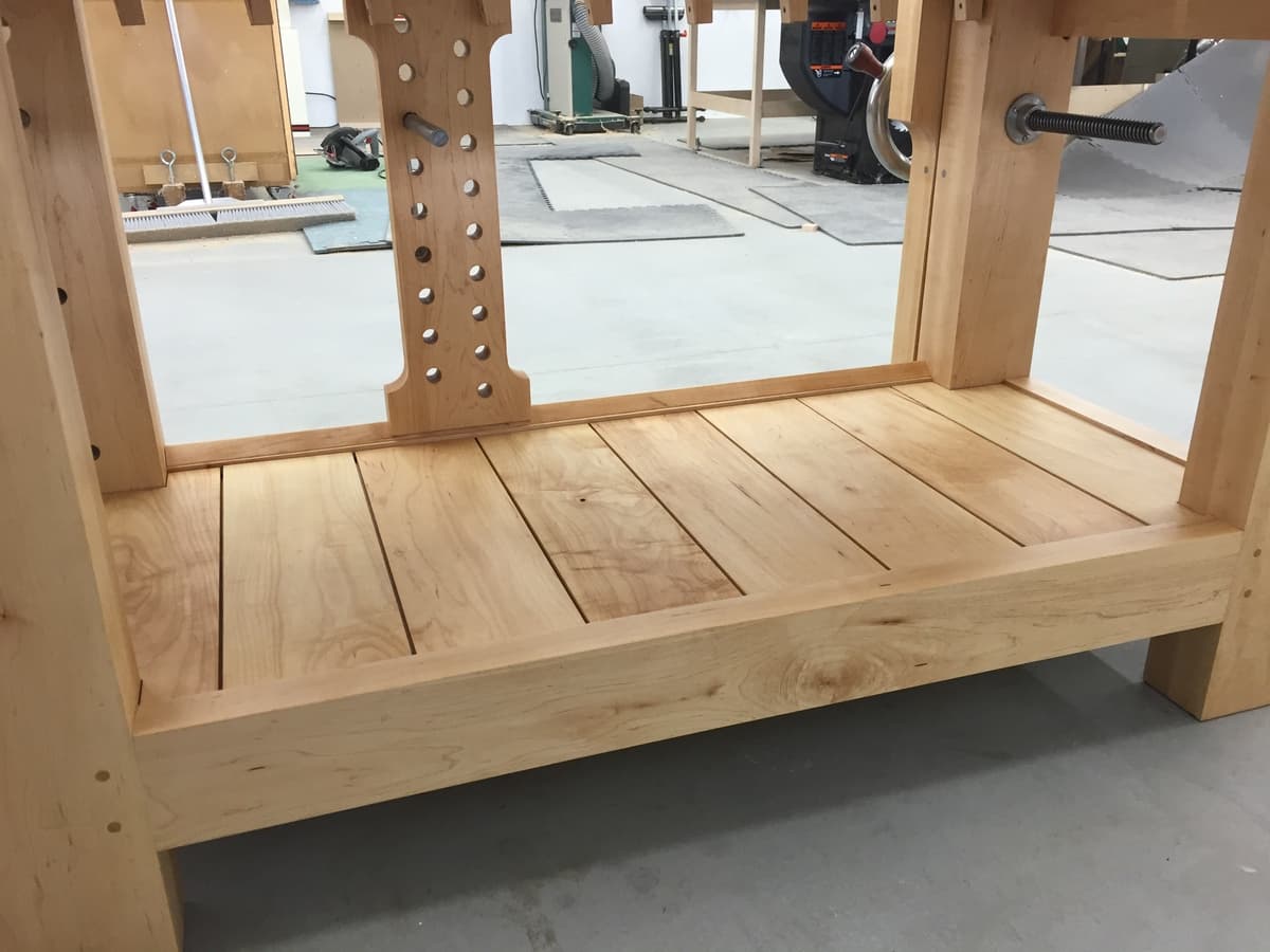 Detail of workbench underside showing slatted maple shelf construction and dog hole pattern in benchtop