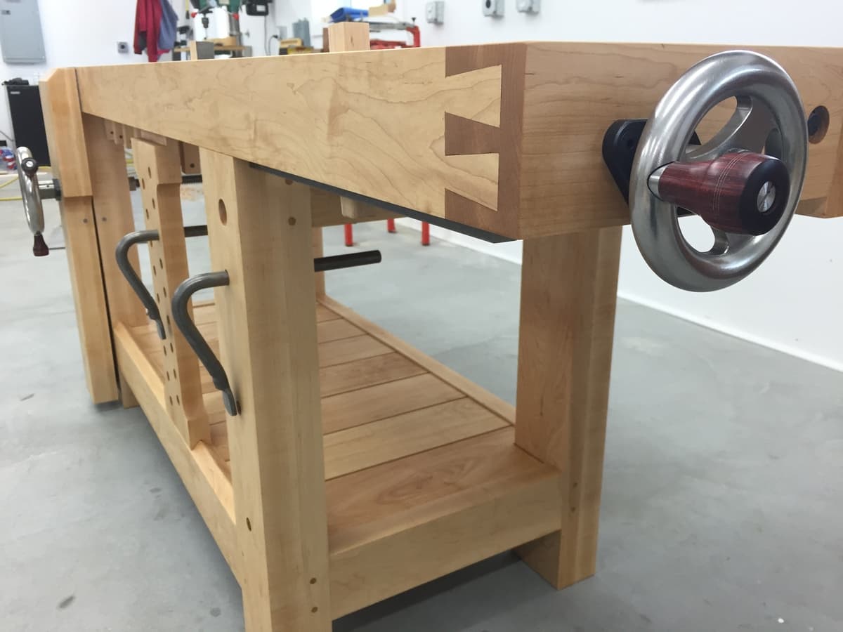 Side view showing leg vise assembly with metal handwheel, wooden handle grips, and X-stretcher joint detail