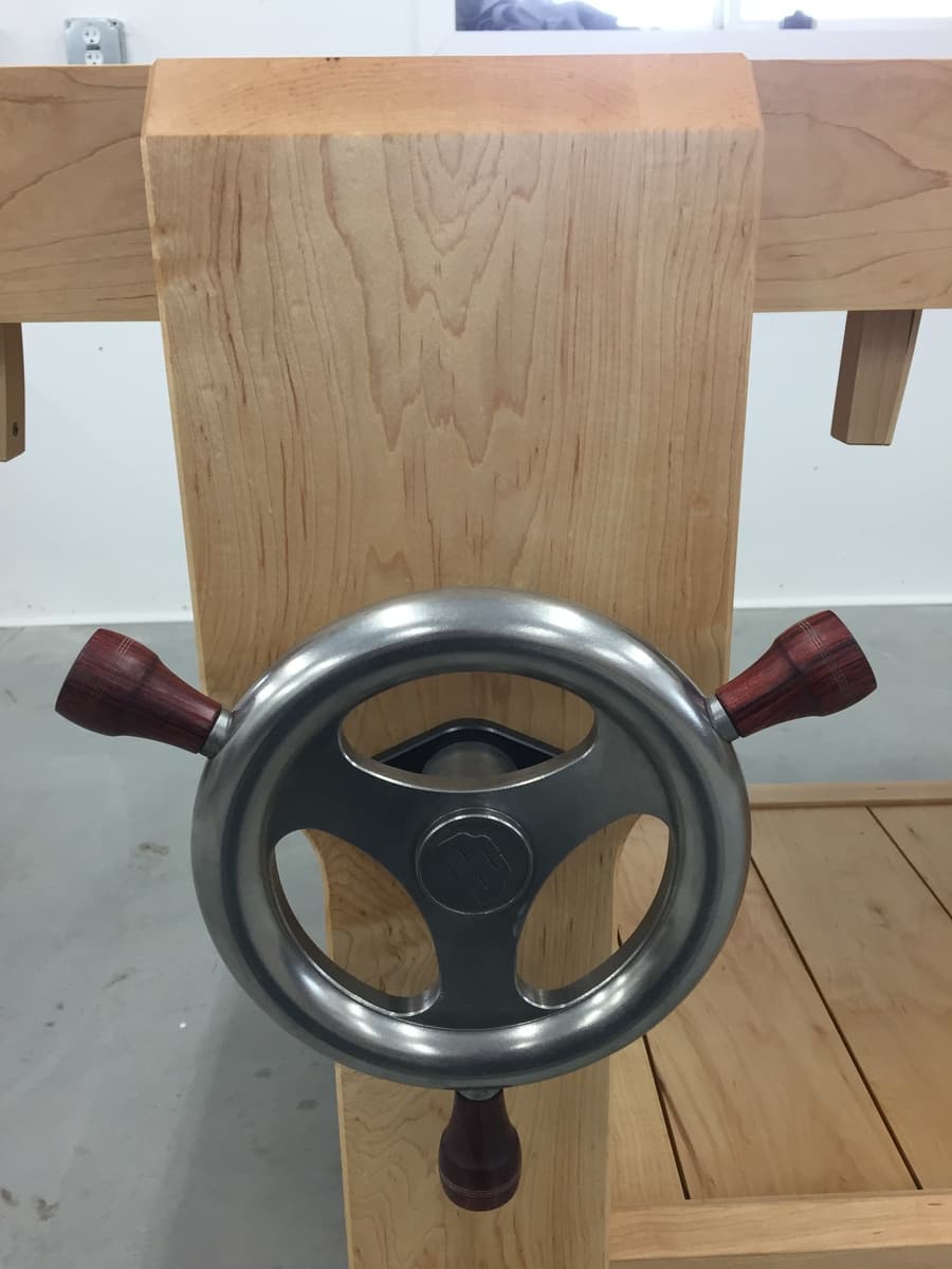 Top-down view of leg vise handwheel with burgundy wooden handles against hard maple benchtop grain