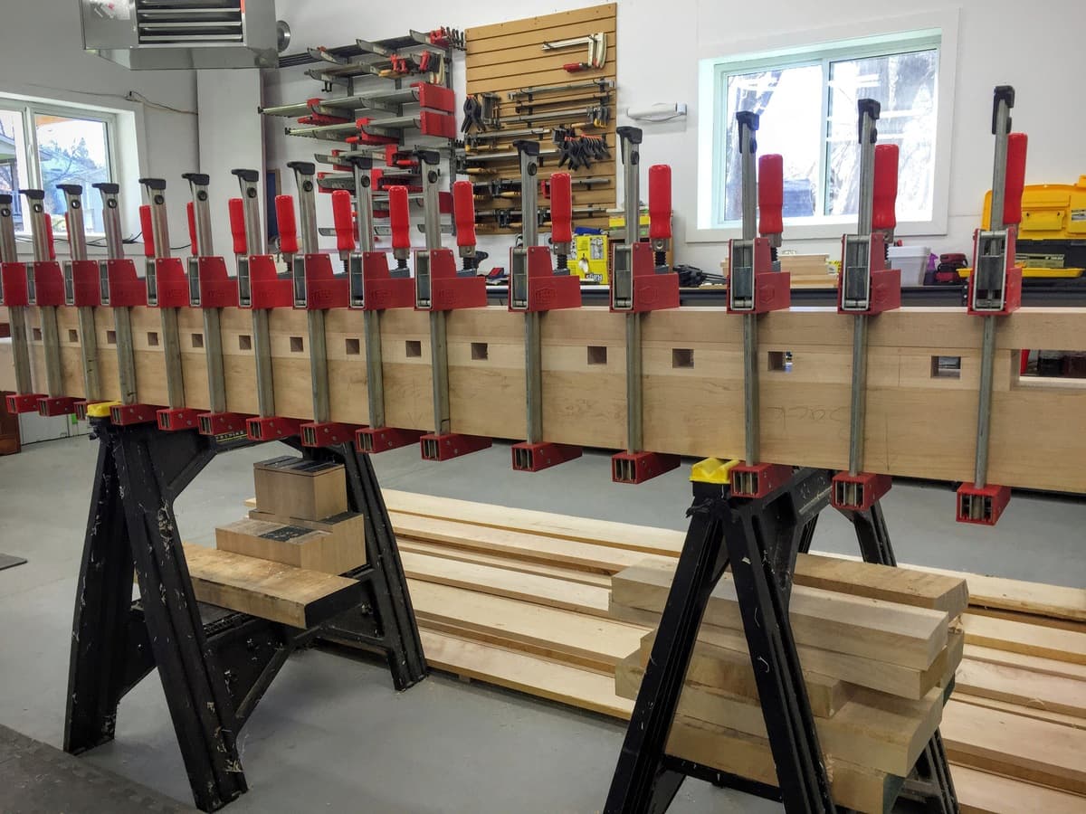 Multiple maple benchtop slabs clamped with red Bessey clamps during edge-gluing, showing dog hole layout