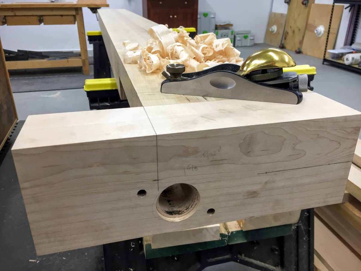 Benchtop slab supported on sawhorses showing dog hole mortises cut along front edge with fresh sawdust on shop floor