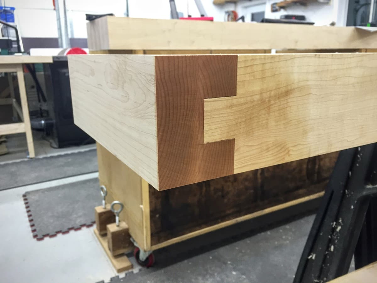 Hand plane with brass accents and curled maple shavings resting on workbench leg during surface preparation